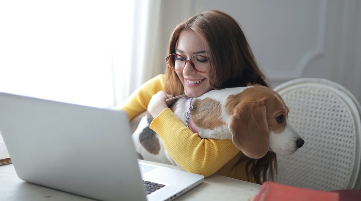 A young woman holding her dog in her lap while she browses the internet on her laptop