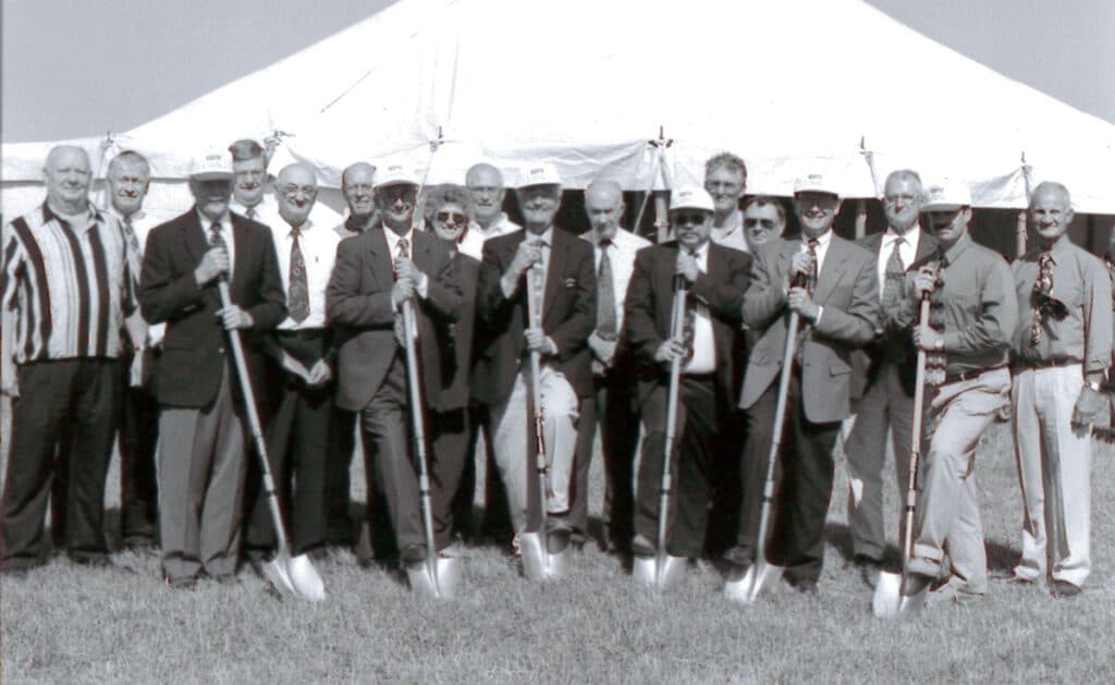Black & white photo of NDTC employees posing with shovels at a groundbreaking ceremony