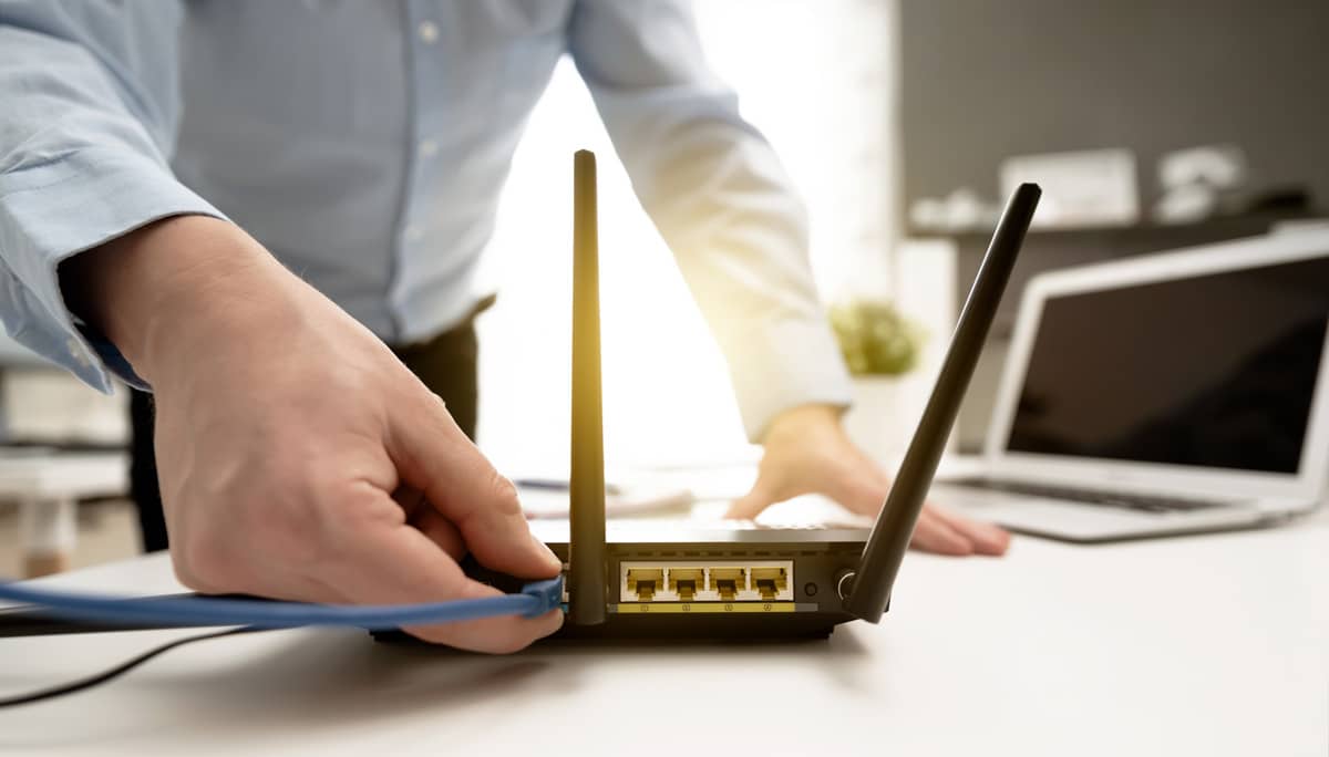 A closeup of a man plugging an ethernet cable into an internet router