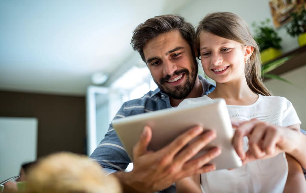 A father and daughter looking at a tablet together in their home