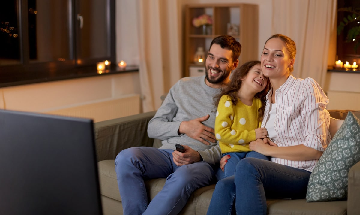 A dad, mom, and daughter watching TV together in a modern living room