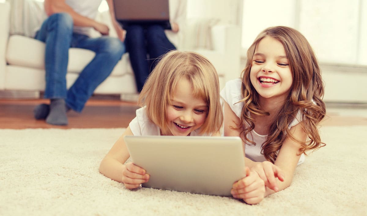 Two young girls are laughing while watching a TV show on a tablet