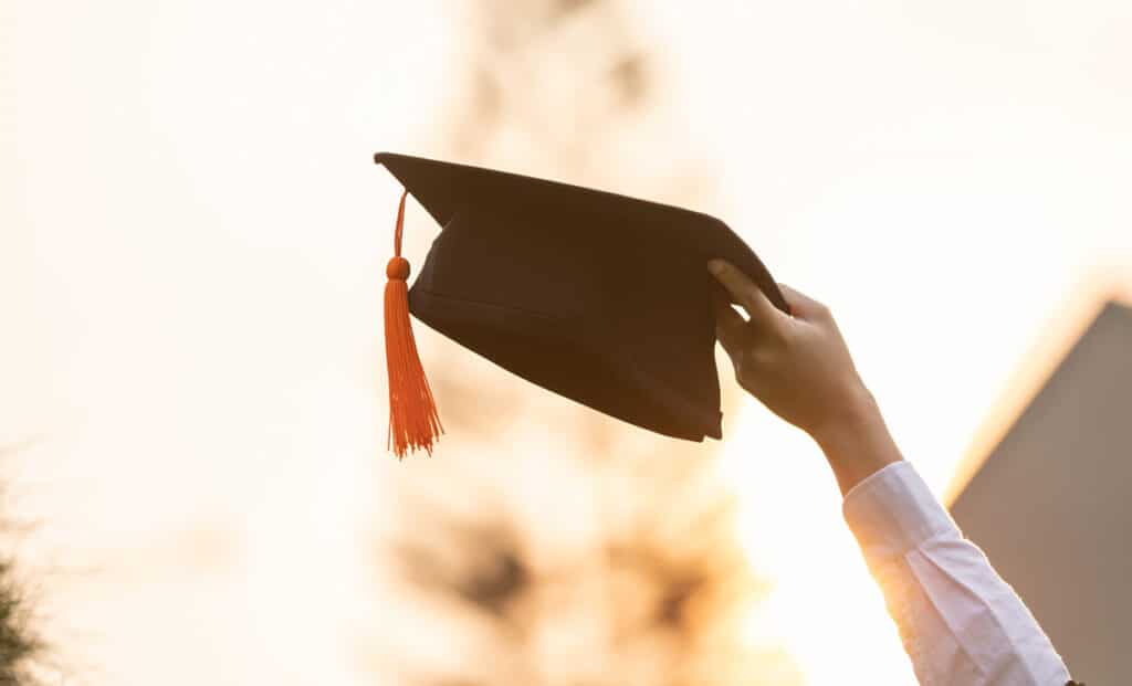 A person holding up a black graduation cap