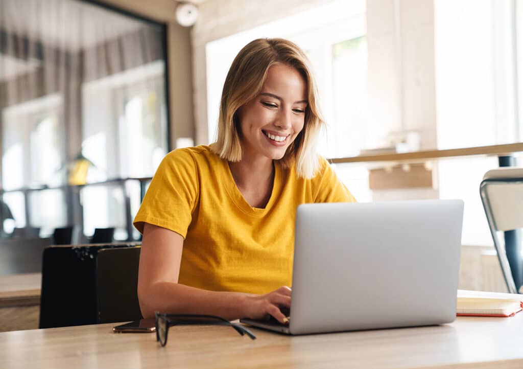 A young woman smiling as she's working on a laptop